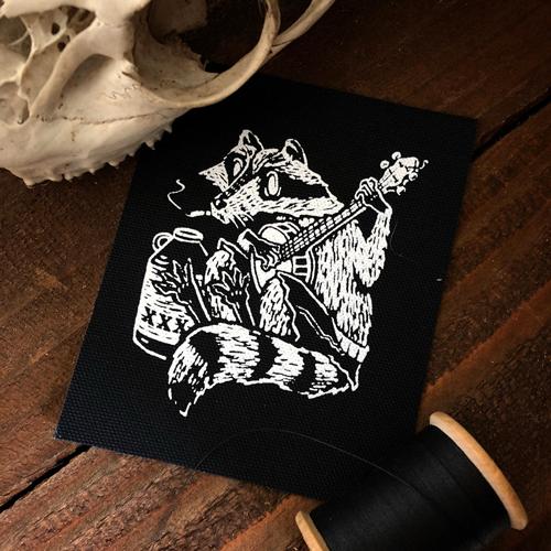Racoon playing banjo next to jug in white ink on black rectangle sew on patch. Art by Collin Hammin.